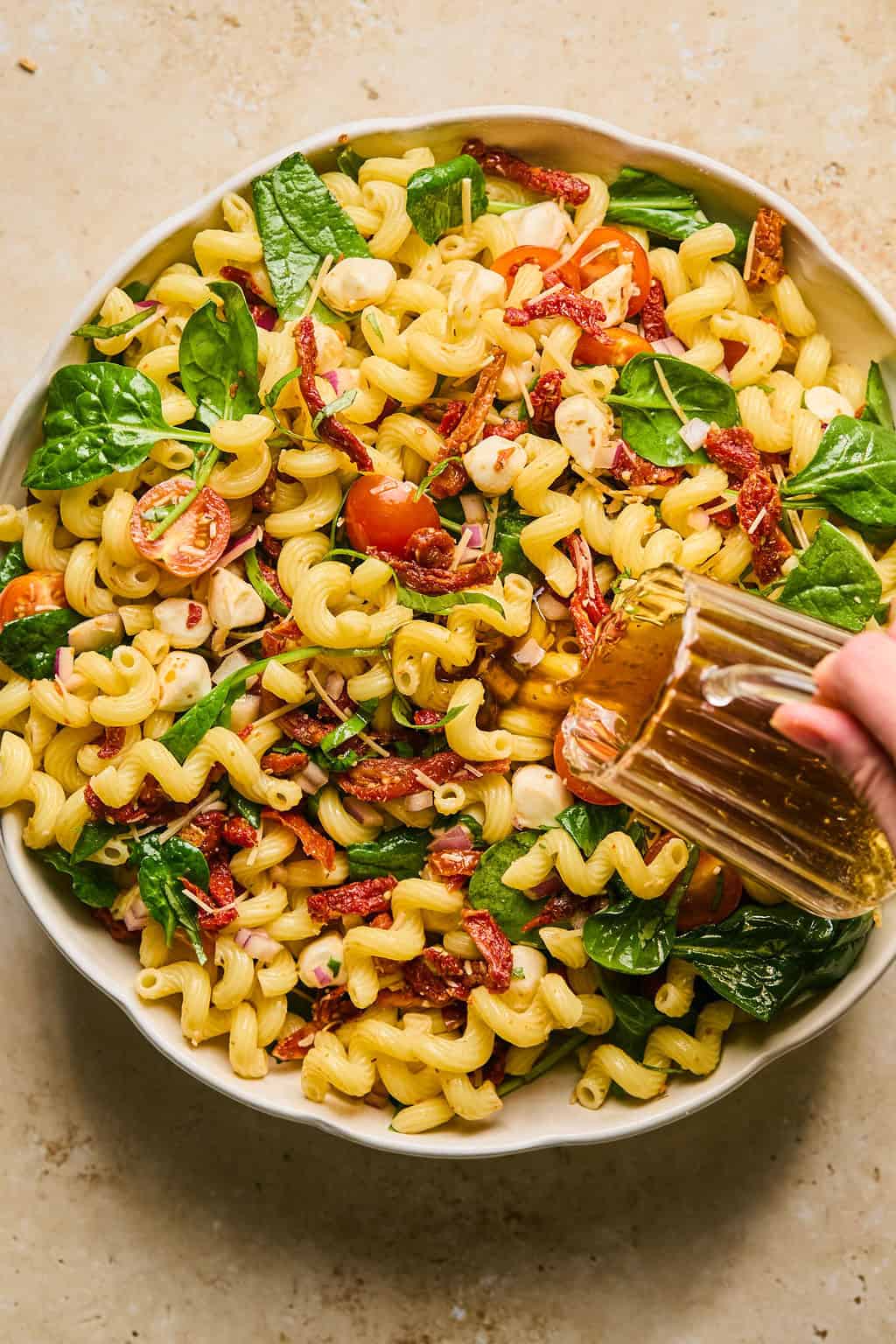 Pasta salad with dressing being poured over top.
