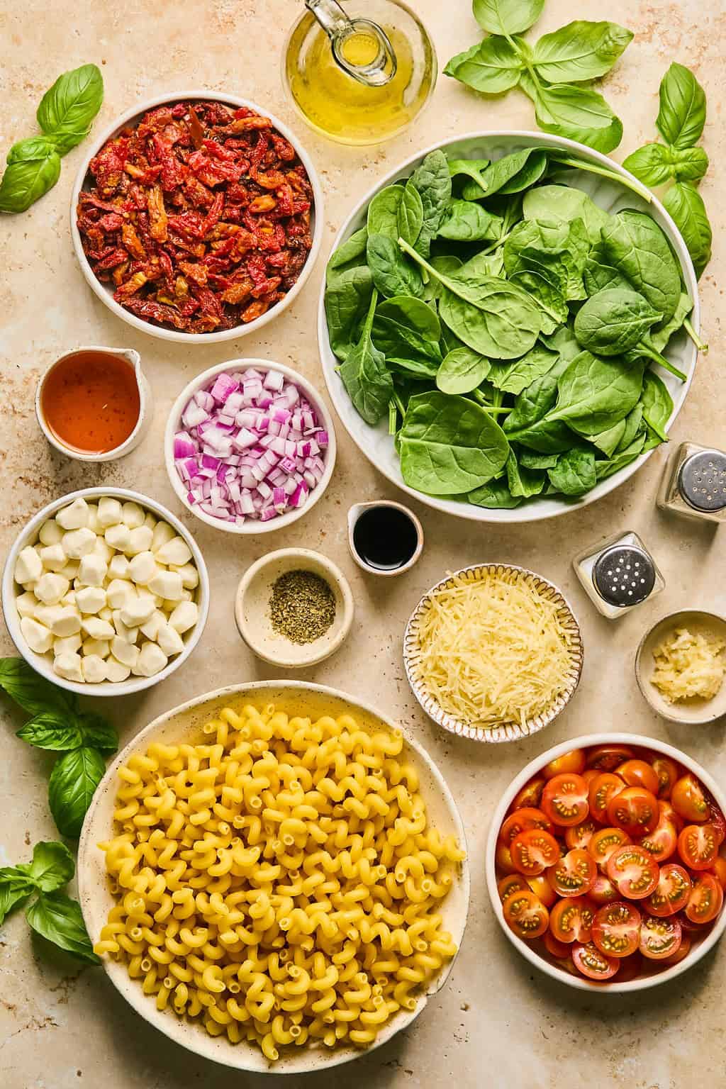 Spinach, pasta, parmesan cheese, olive oil and other ingredients arranged on surface.