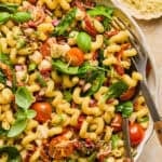 Sun dried tomato pasta salad topped with chopped basil and spoon and fork propped in the bowl.