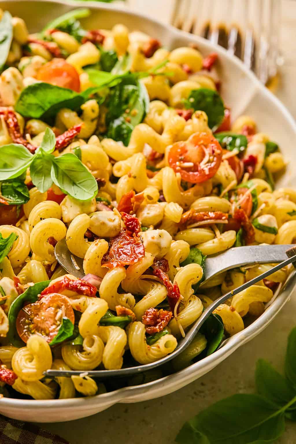 Sun-dried tomato pasta salad in white dish topped with freshly chopped basil.
