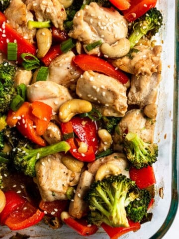 Cashew chicken in glass baking dish with peppers and broccoli topped with sesame seeds.