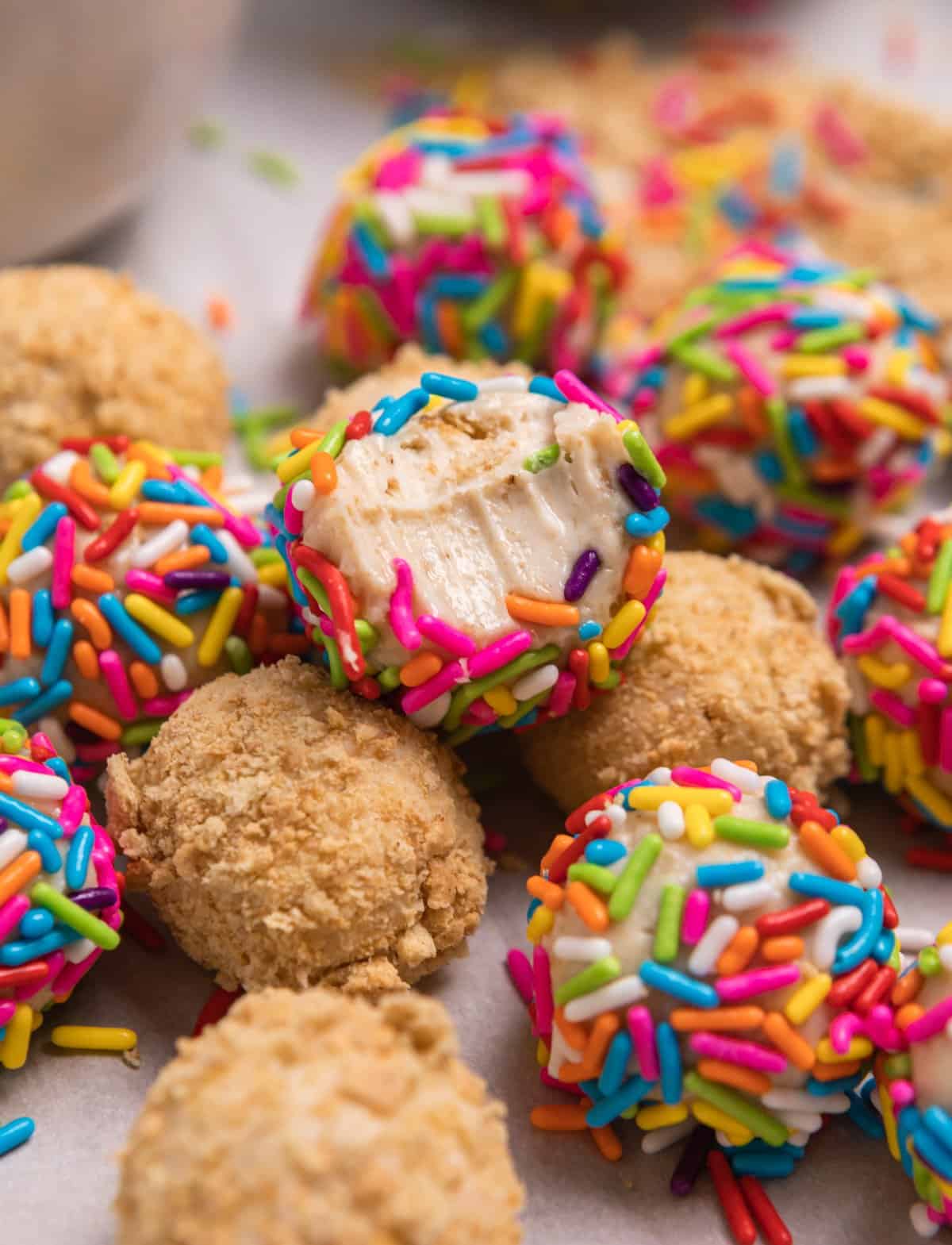 Cheesecake balls covered in sprinkles and crushed graham crackers with bite taken out of one ball.