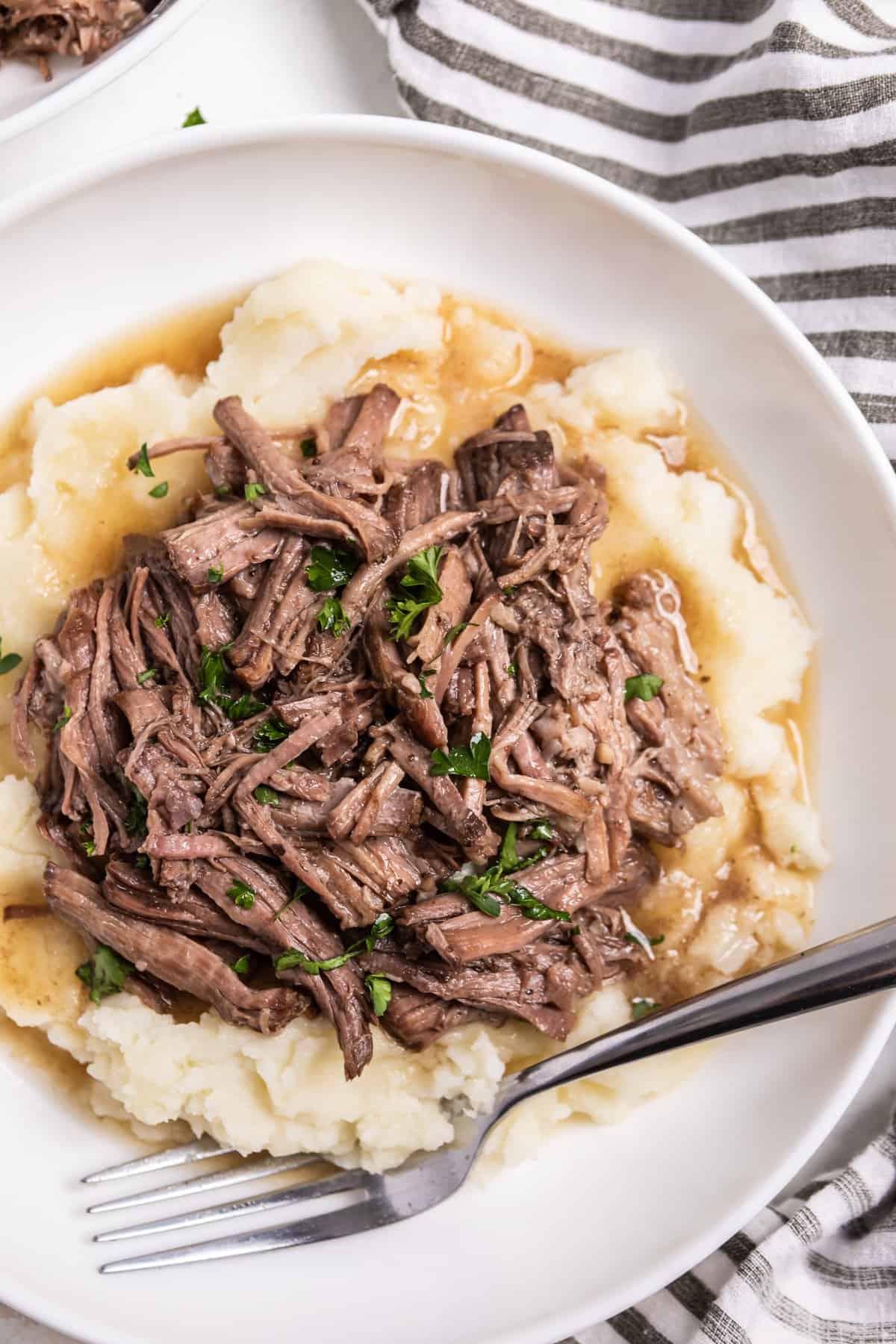 White dish with mashed potatoes topped with crock pot shredded beef.