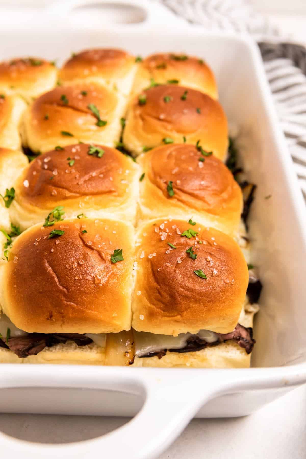 White baking dish with fresh French dip sliders topped with parsley.