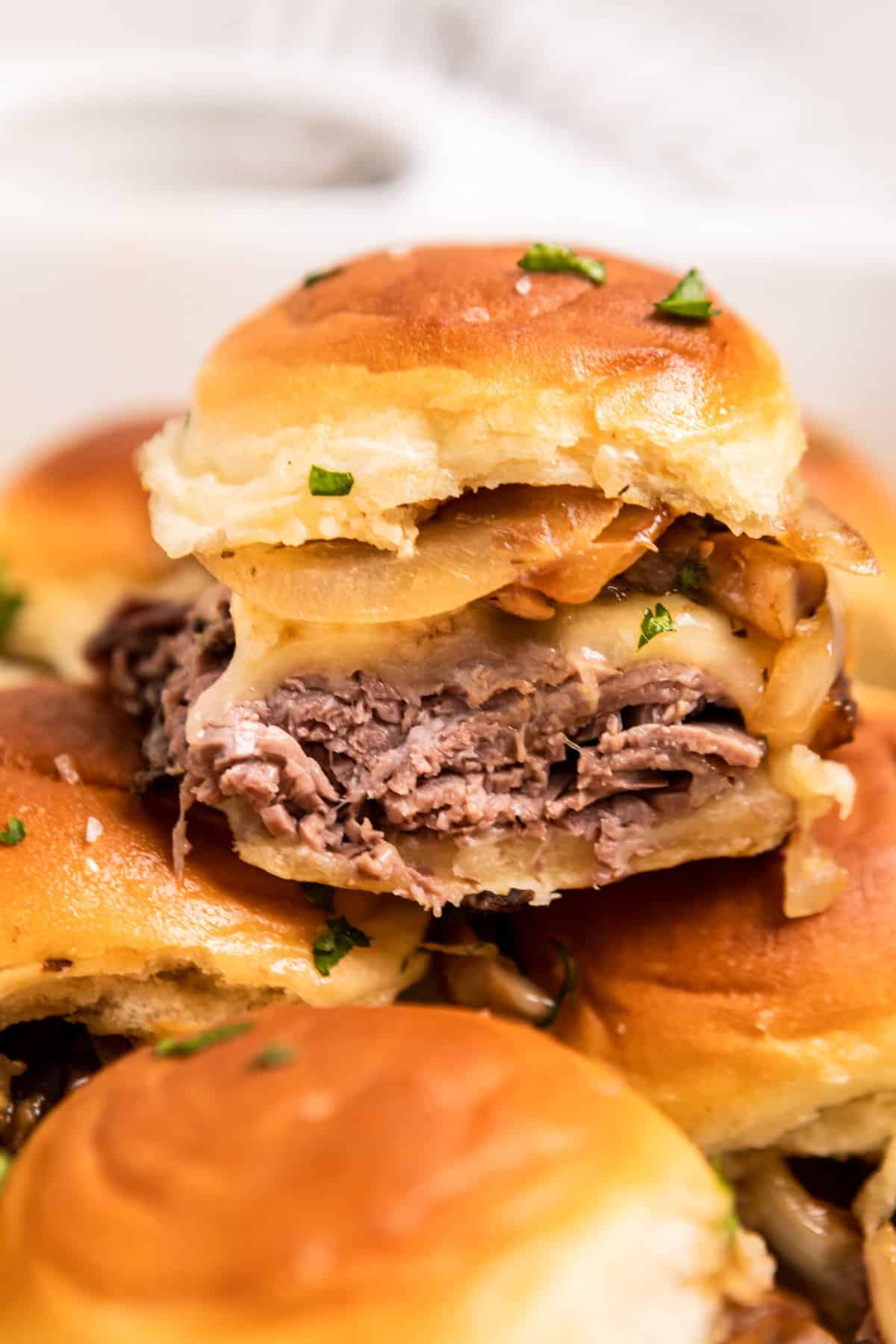 French dip slider with roast beef, provolone, onion and mushroom stacked on other sandwiches.