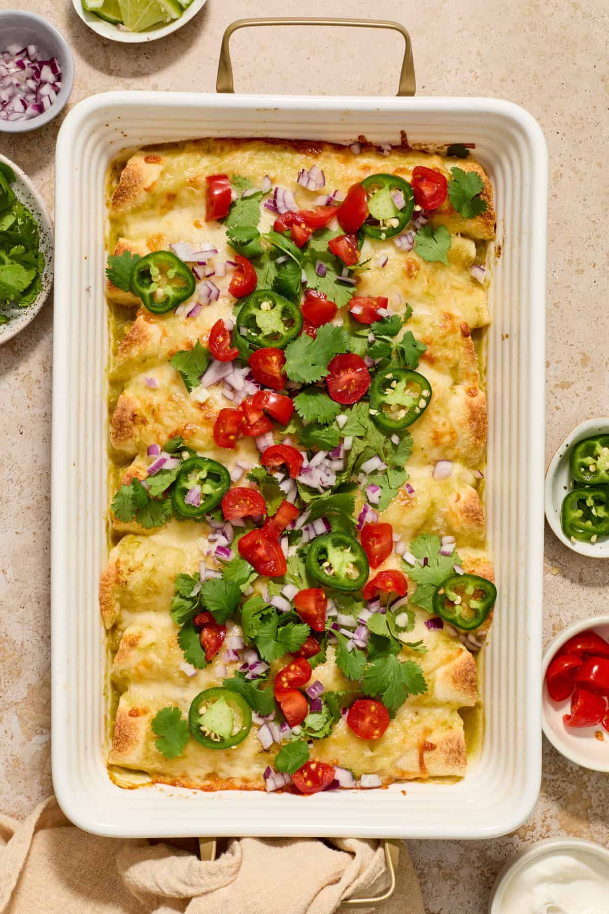Pan with chicken enchiladas in green sauce with melted cheese and chopped cilantro on top.