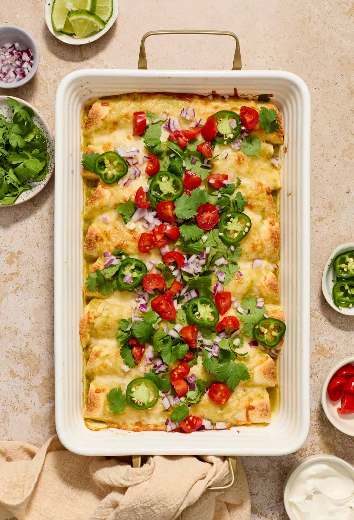 Pan of enchiladas topped with tomatoes, onions, cilantro, and jalapeños.
