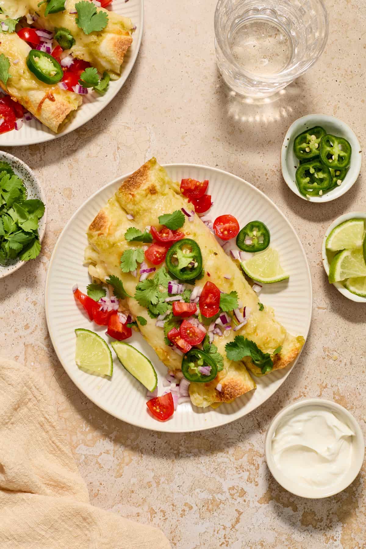 Chicken enchiladas on white plate topped cilantro, tomatoes and jalapeños.