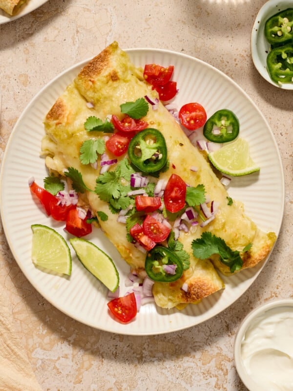 Green chicken enchiladas on plate with cilantro and other toppings.