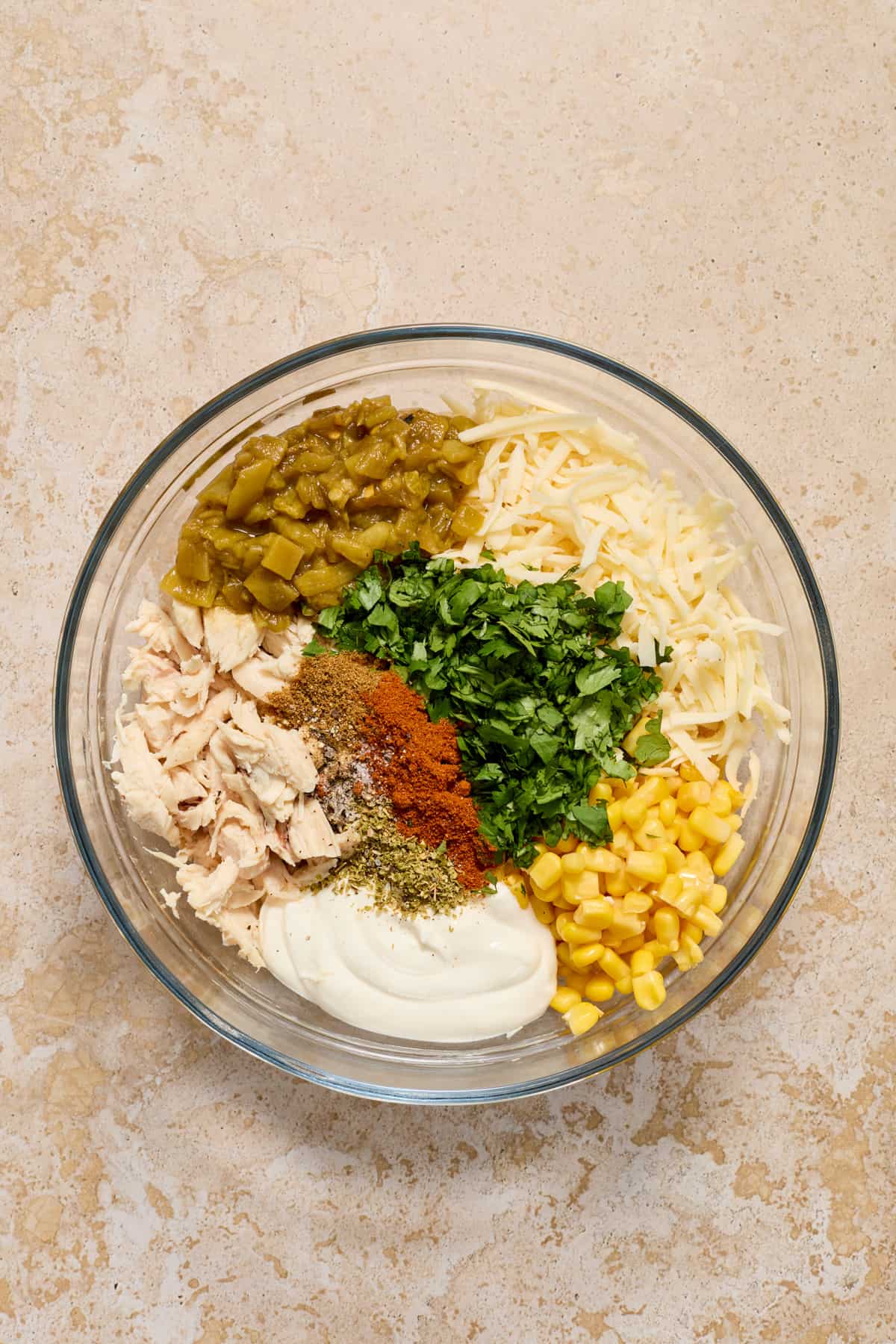 Chicken, cilantro, corn, spices, sour cream, cheese and other ingredients for chicken enchiladas in bowl.