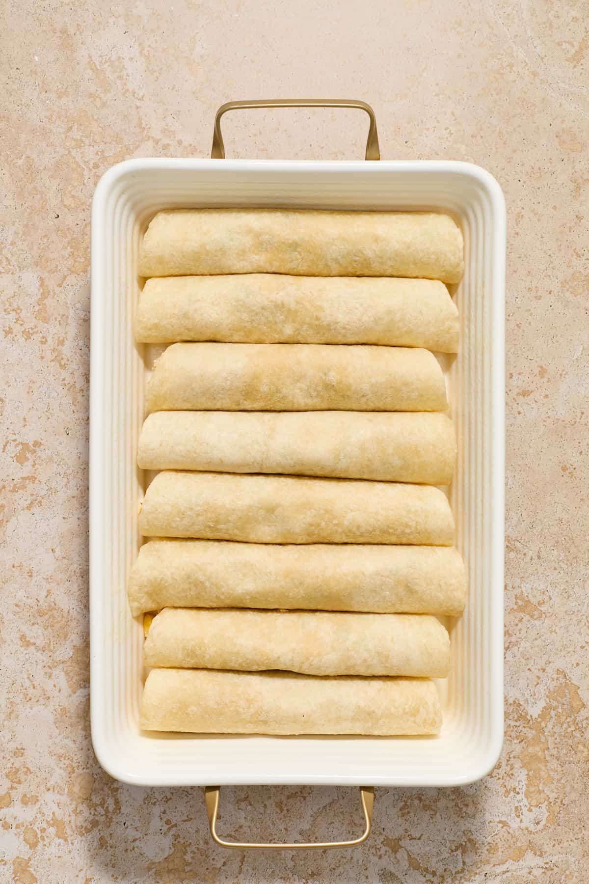 Rolled tortillas with green chicken enchilada mixture in pan.