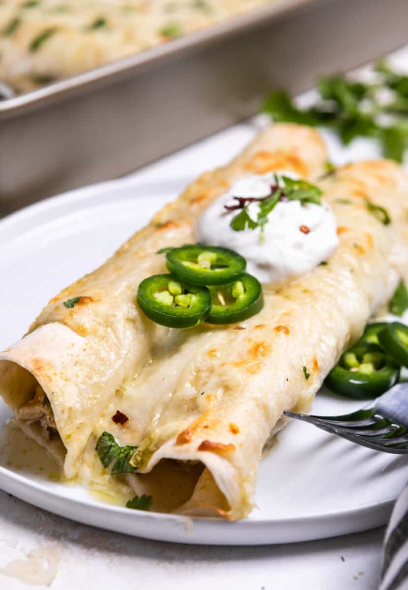 Chicken enchiladas on white plate topped with sour cream and jalapeños.