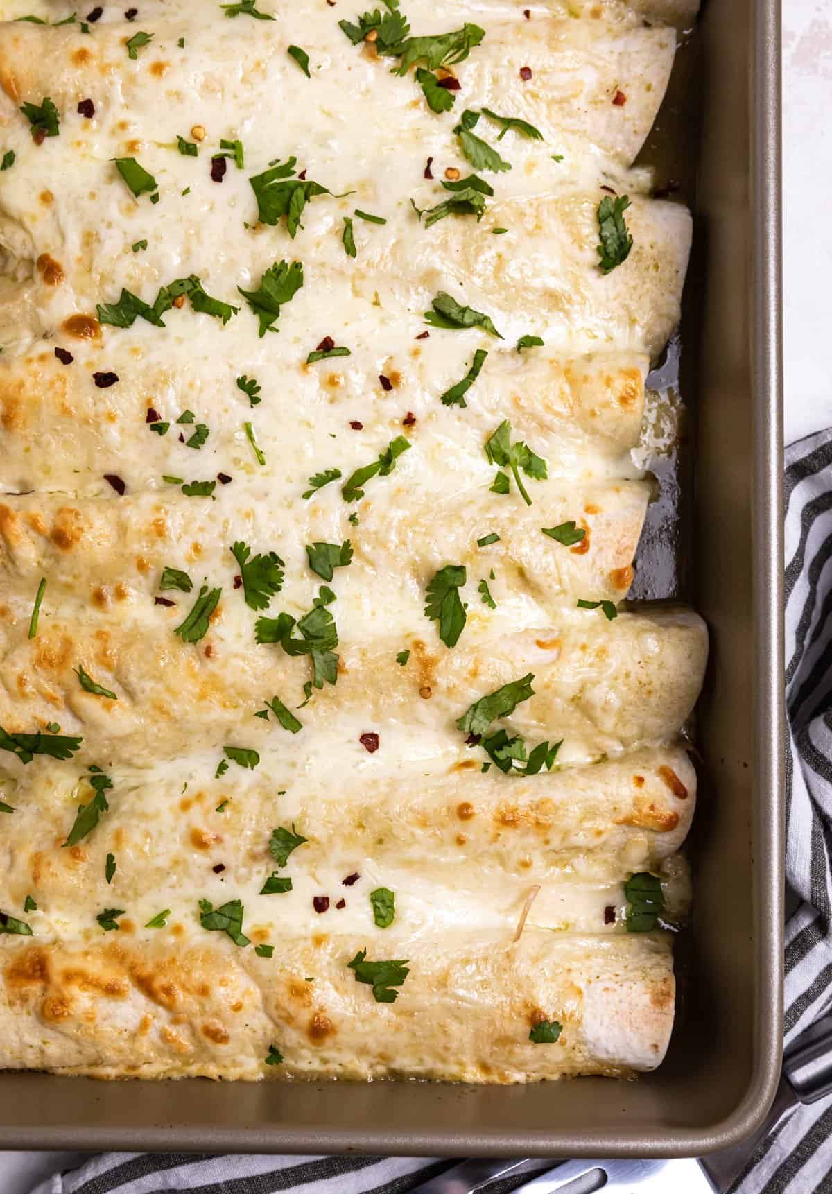 Baked green chicken enchiladas with chopped cilantro on top in baking pan.