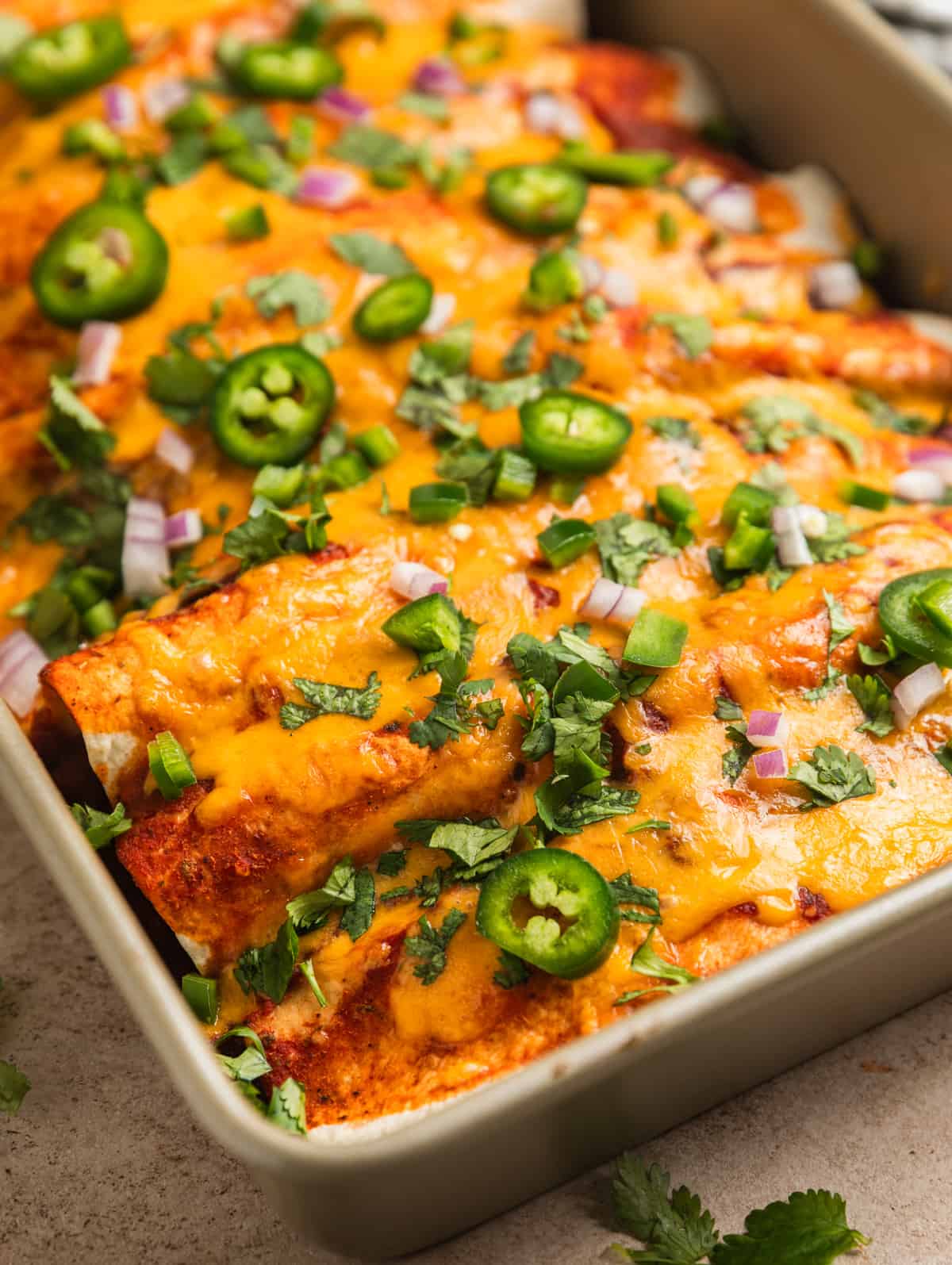 Enchiladas in pan topped with melted cheese and other toppings.