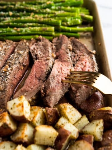 Sheet pan with sliced parmesan flank steak, quartered potatoes and asparagus.