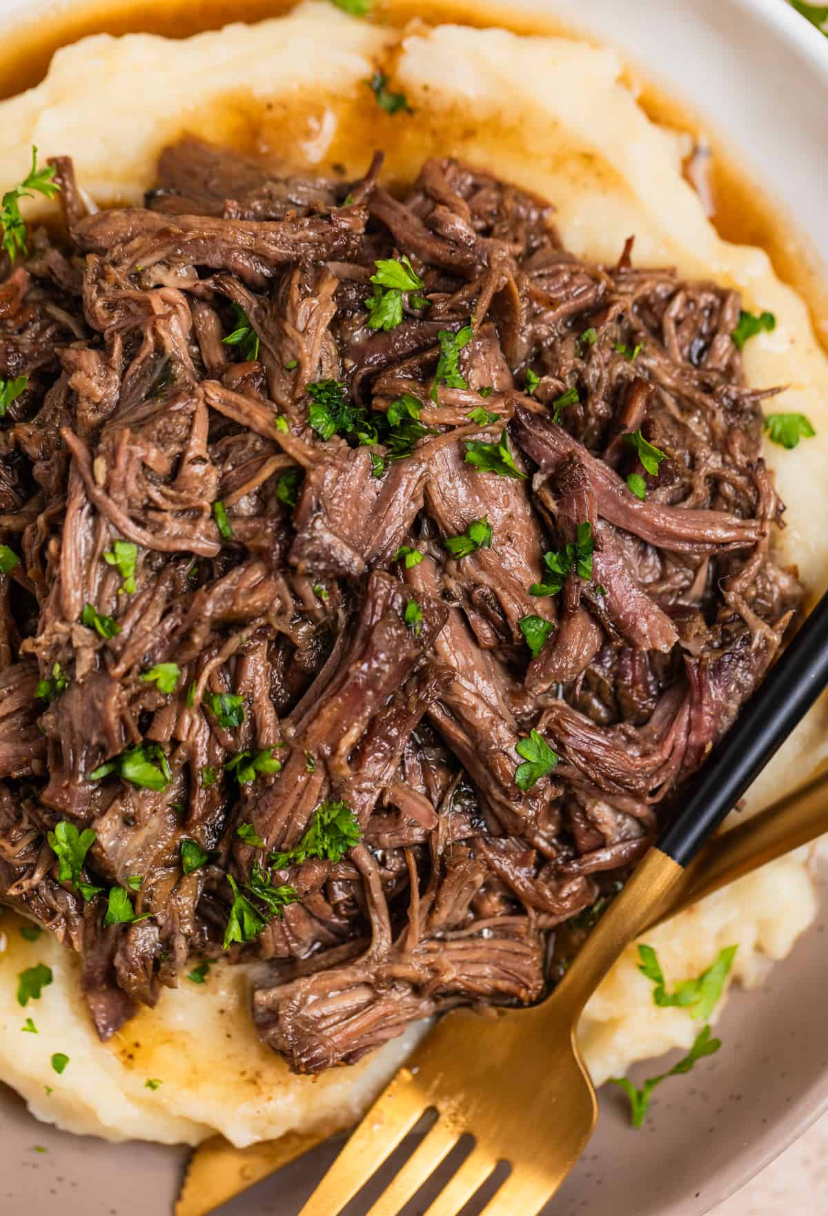 Overhead view of plate with pulled beef in juices over mashed potatoes and topped with chopped herbs.