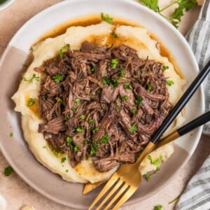 Tan and white plate with crock pot shredded beef over mashed potatoes.