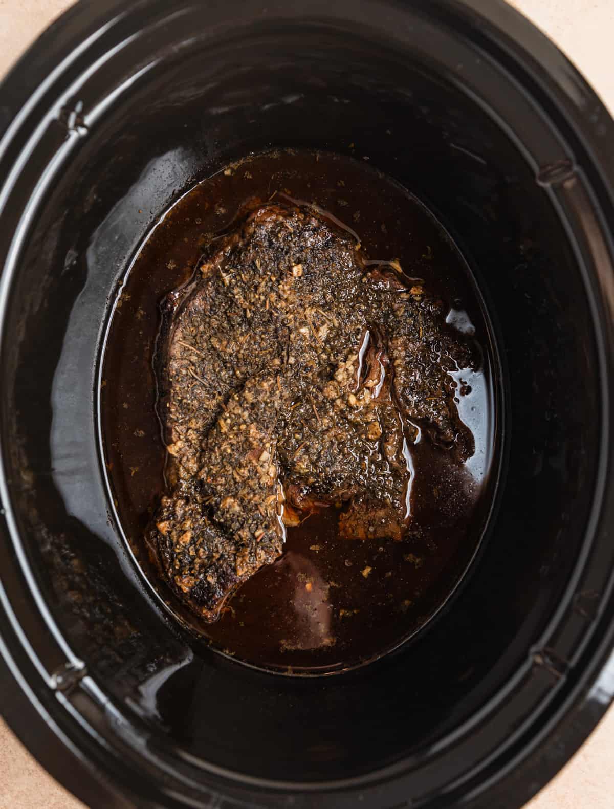 Overhead view of cooked chuck roast in juices in slow cooker.