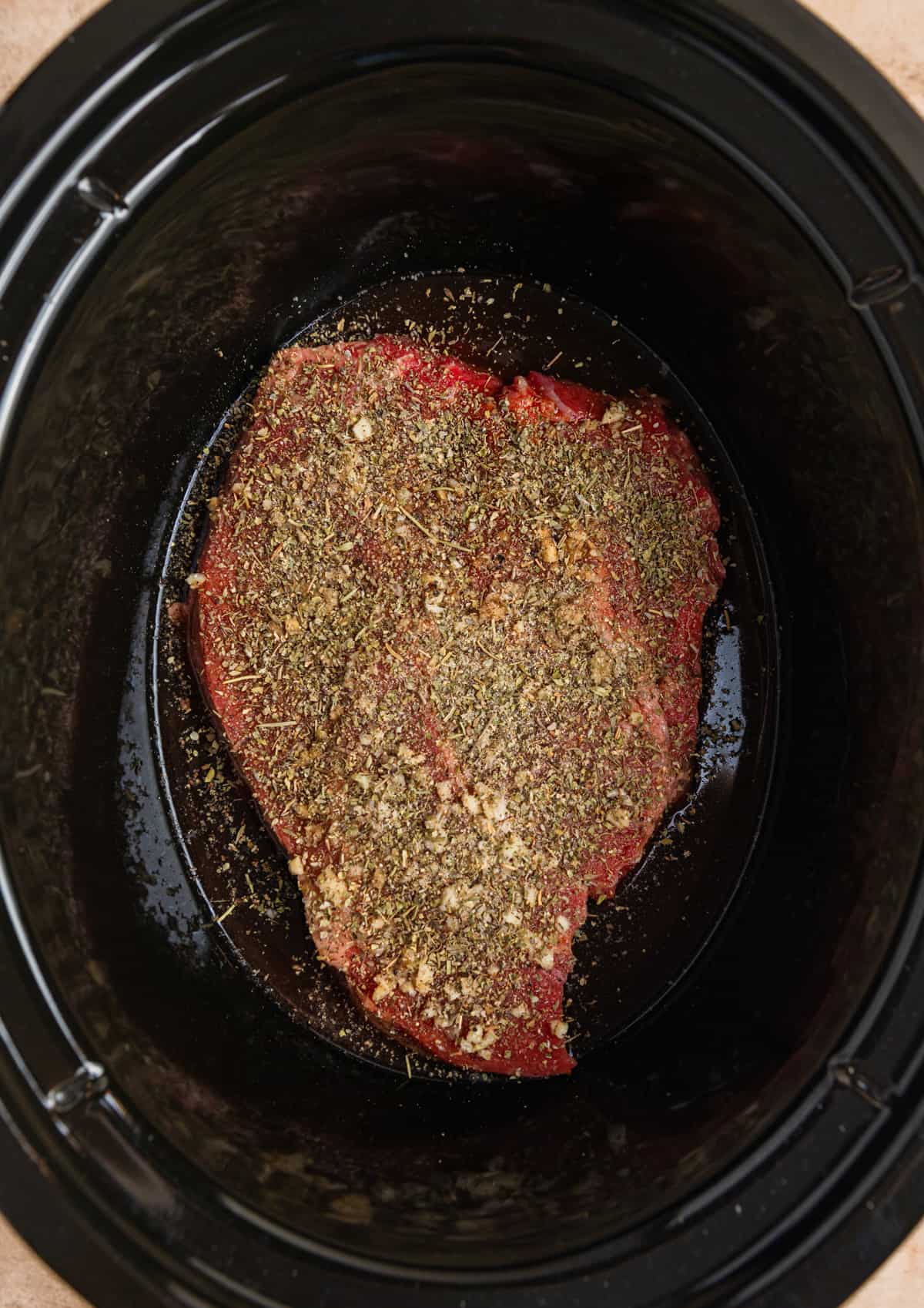Beef chuck roast in crockpot topped with seasoning.
