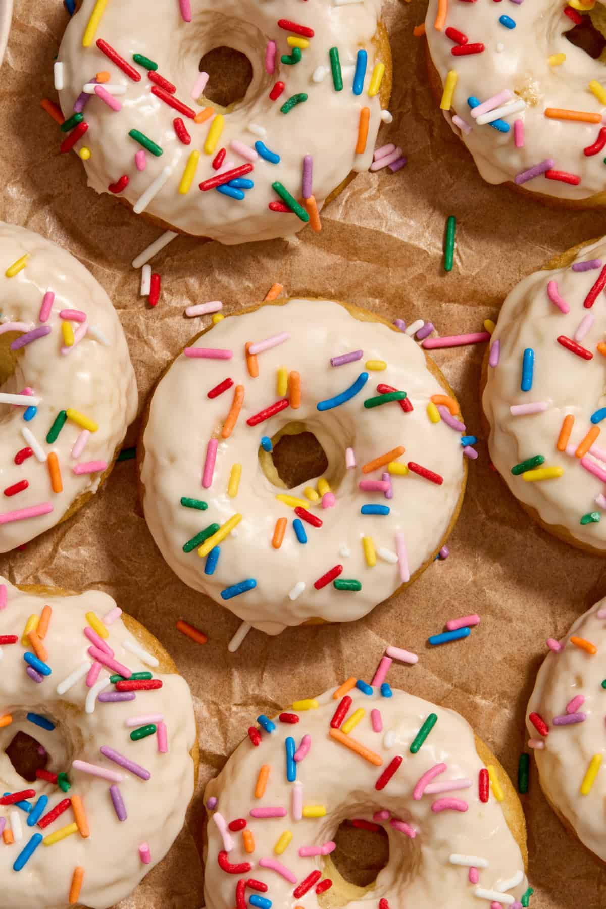 Baked triple vanilla donuts on parchment with rainbow sprinkles.