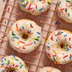 Vanilla donuts on cooling rack with vanilla glaze and sprinkles.