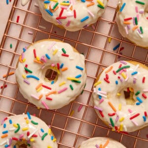 Vanilla donuts on cooling rack with vanilla glaze and sprinkles.