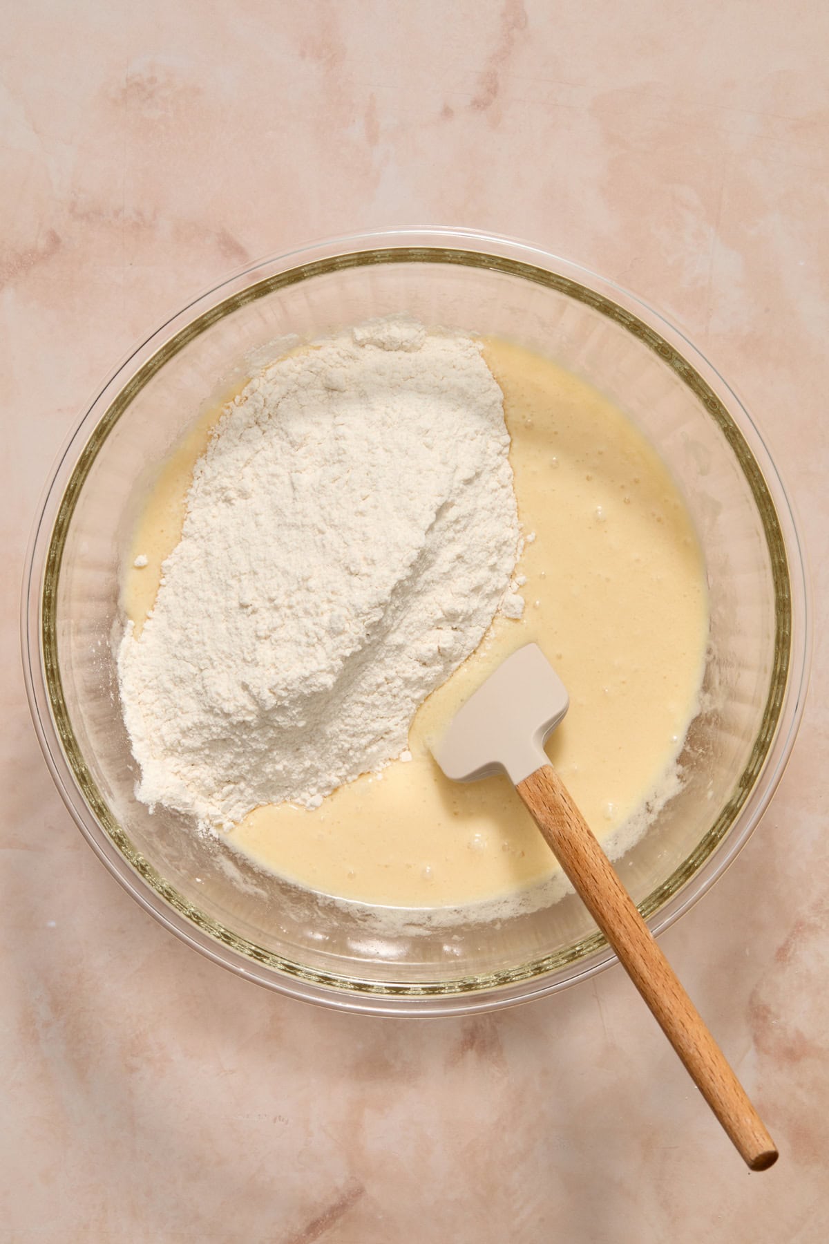 Dry ingredients added to wet ingredients with spatula in bowl.