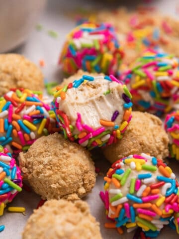 Cheesecake bites with bite taken out and covered in sprinkles and graham cracker crumbs.