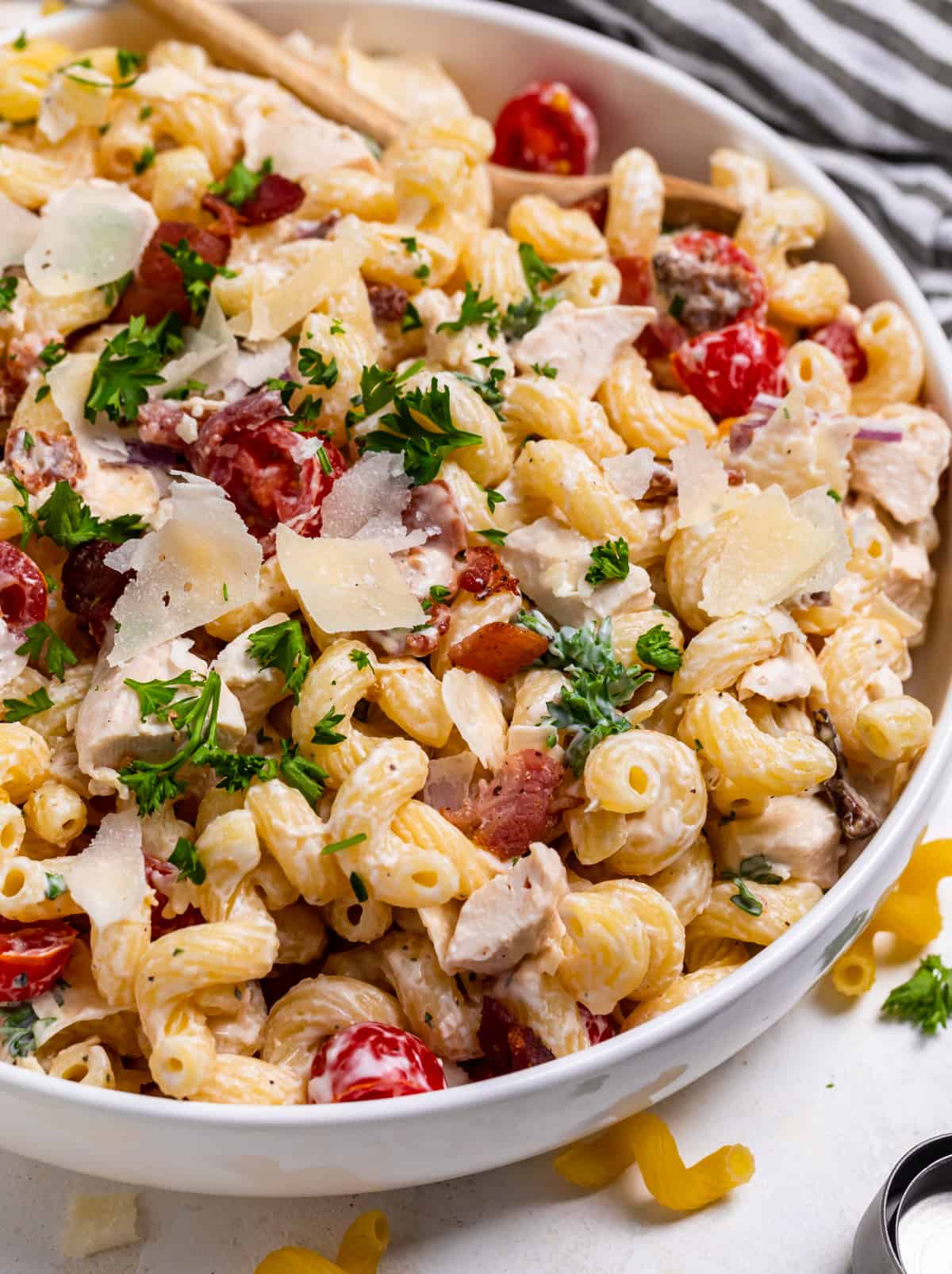Chicken bacon ranch pasta salad in white serving dish topped with shaved parmesan and fresh parsley.