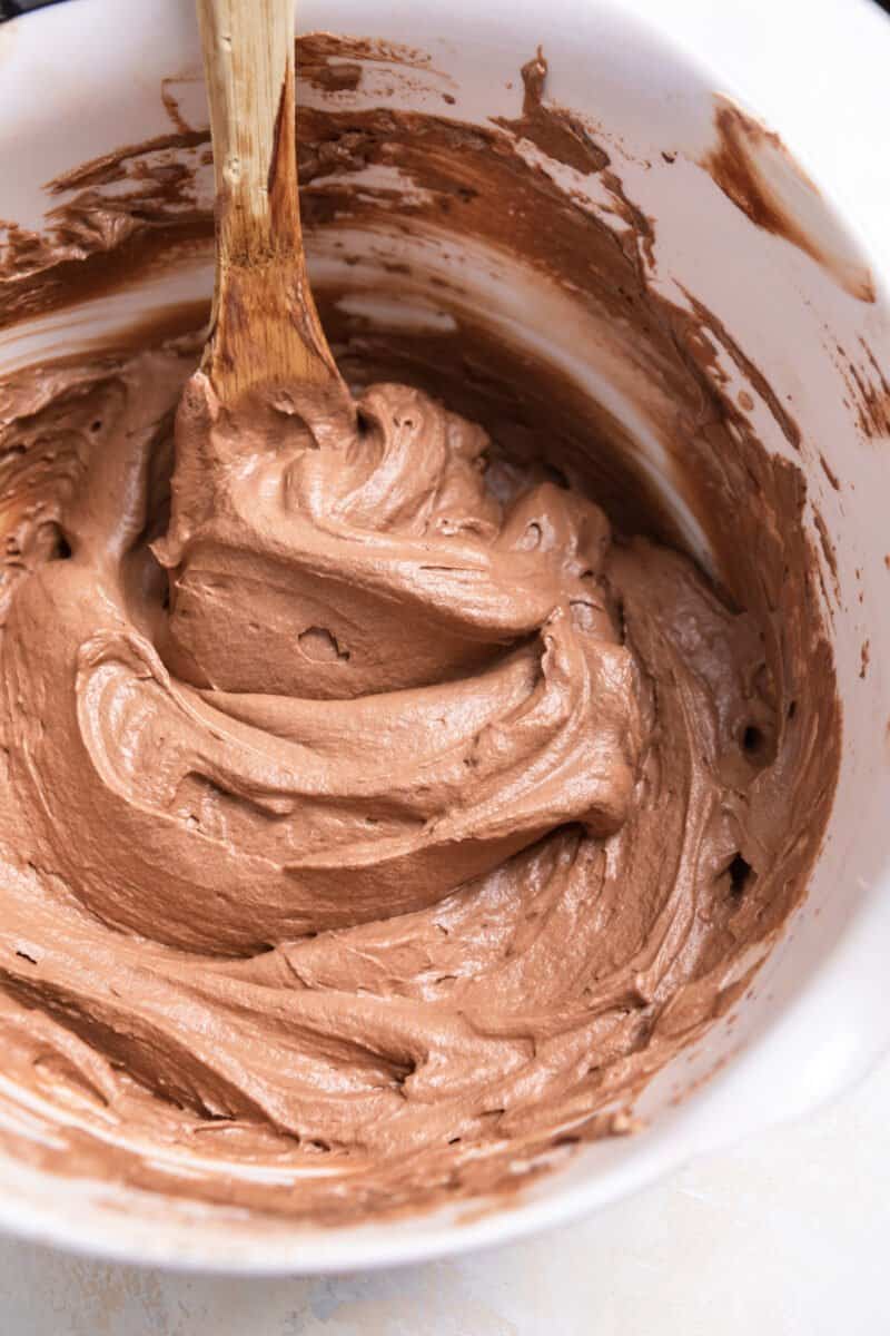 Chocolate cream mixture in mixing bowl with wood spoon.