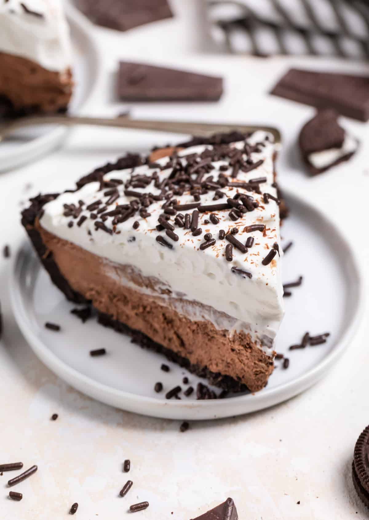 Slice of chocolate cream pie on white dish with sprinkles and Oreos surrounding.