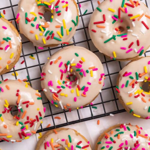Vanilla baked donuts with maple glaze and rainbow sprinkles on cooling rack.