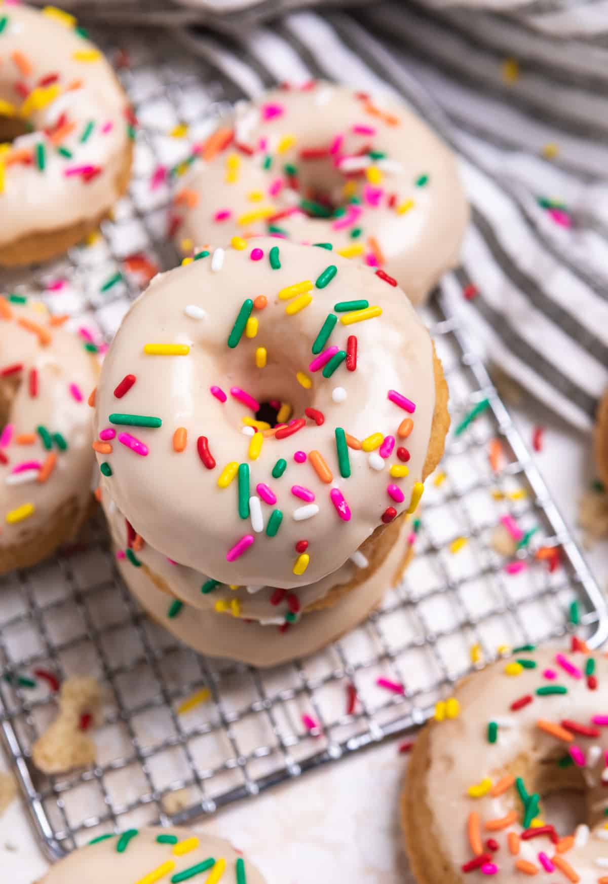 Stack of vanilla donuts with icing and rainbow sprinkles.