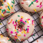 Vanilla donuts on cooling rack with glaze and rainbow sprinkles.