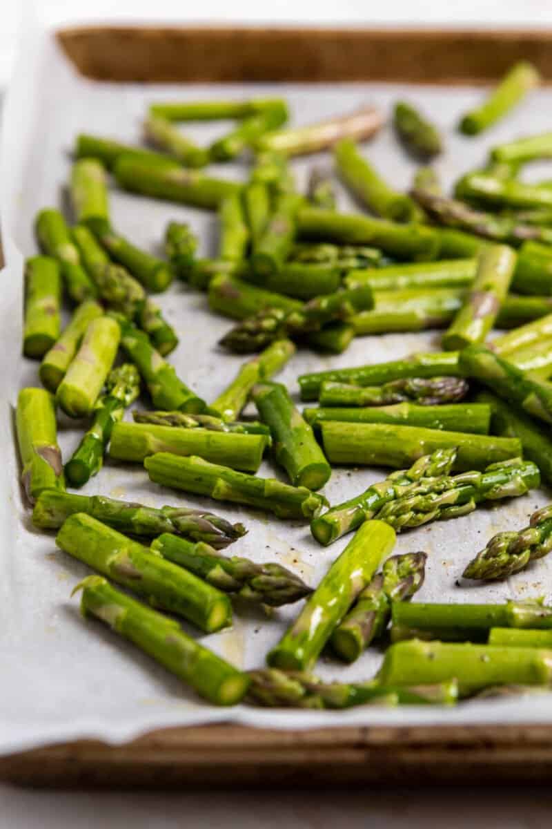 Sheet pan with asparagus chopped and seasoned for roasting.