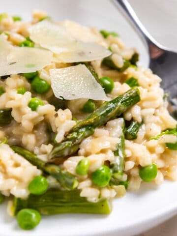 White dish with pea and roasted asparagus risotto topped with freshly shaved parmesan.
