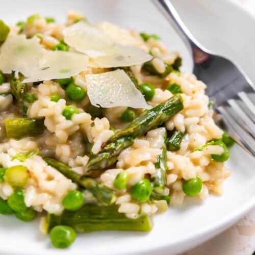 White dish with pea and roasted asparagus risotto topped with freshly shaved parmesan.