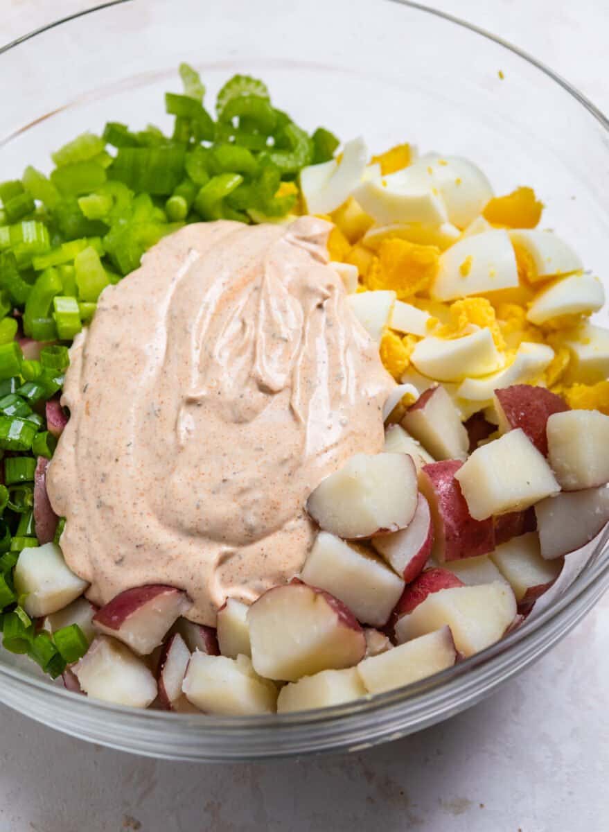 Cooked potatoes, celery, chopped eggs, dressing and other cajun potato salad ingredients in glass dish.