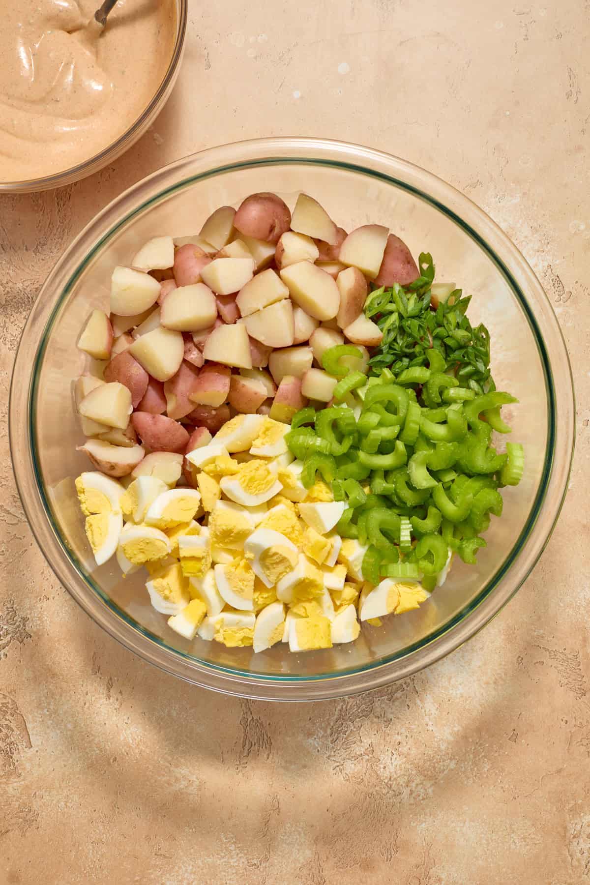 Boiled potatoes, chopped eggs, celery and onion in glass bowl before tossing.