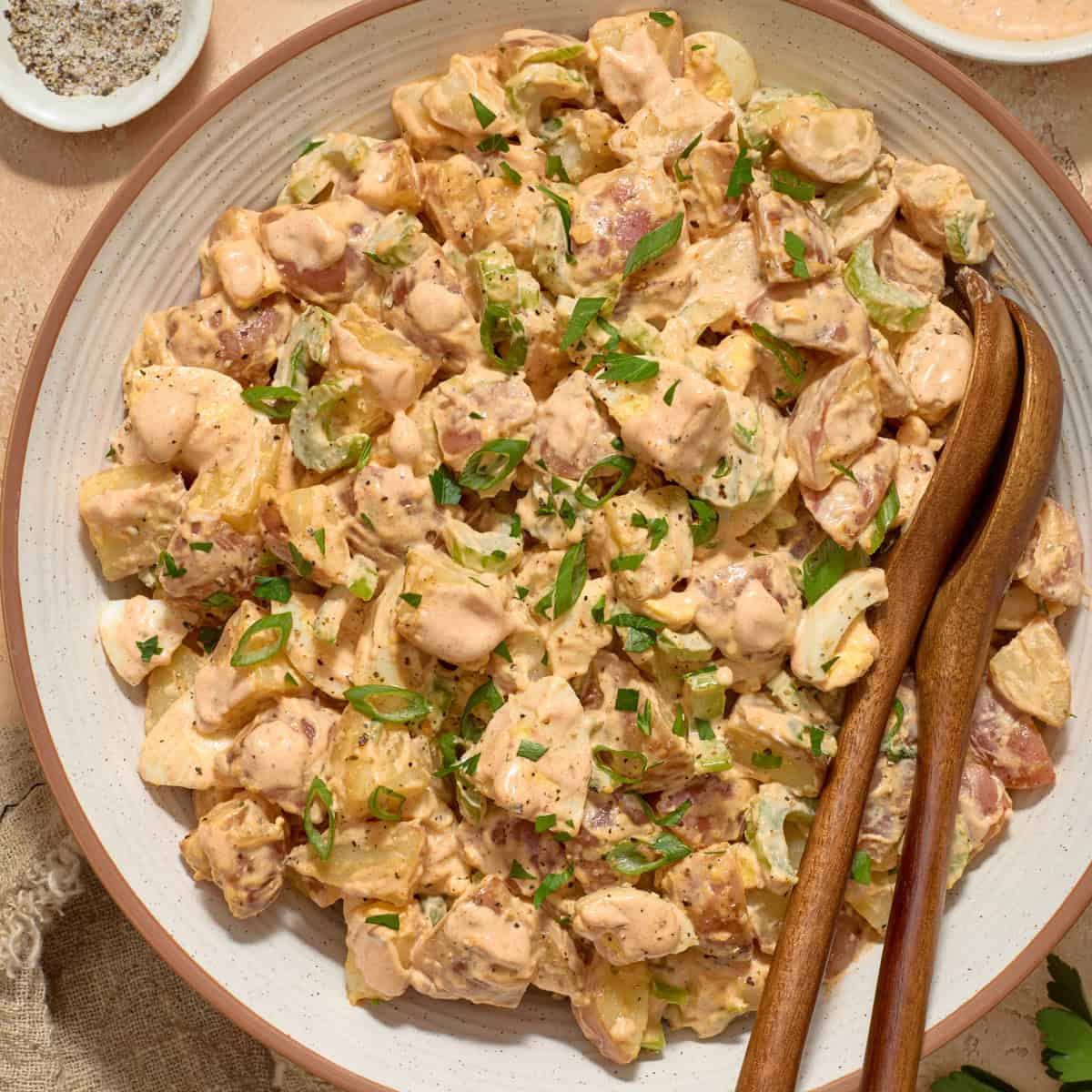Serving bowl with potato salad and serving utensils.