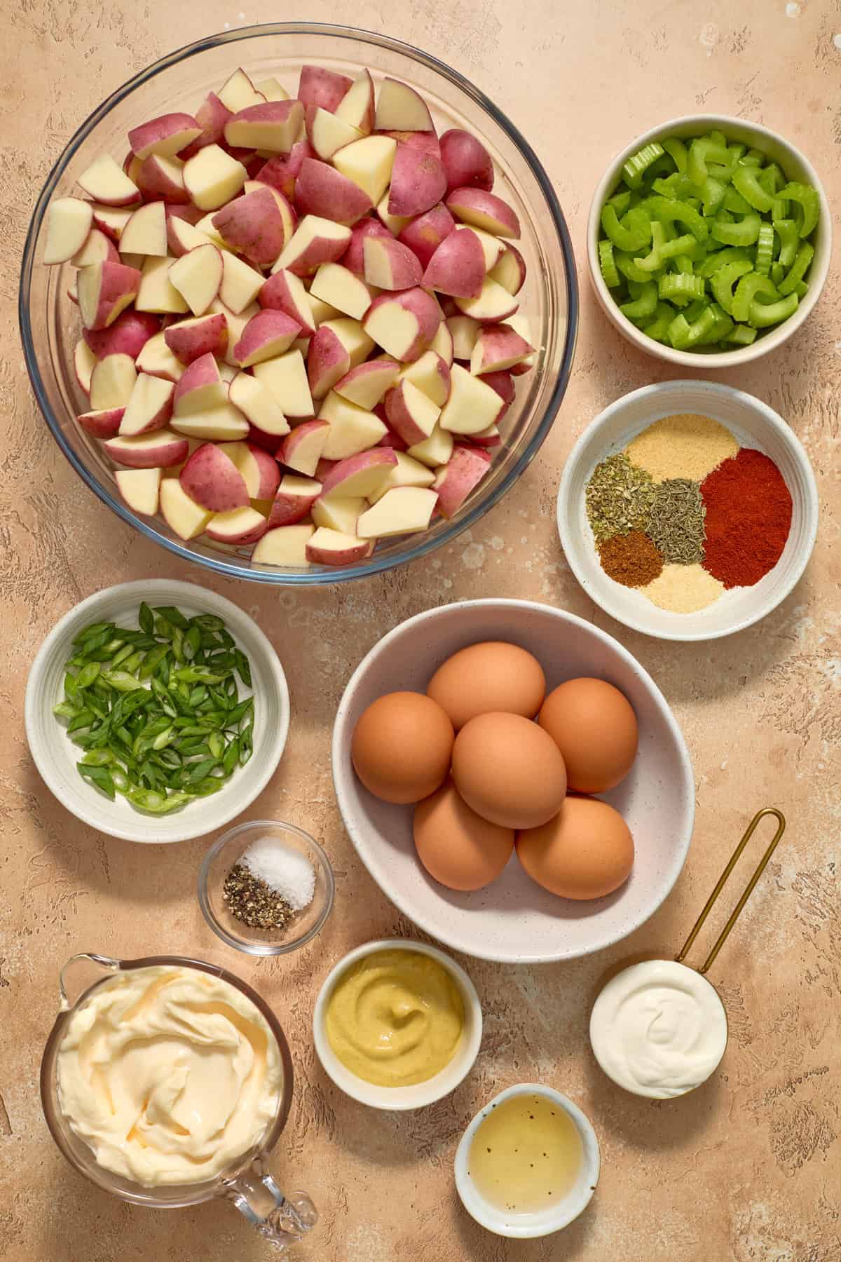 Potatoes, eggs, celery, mayo and other ingredients arranged on surface.