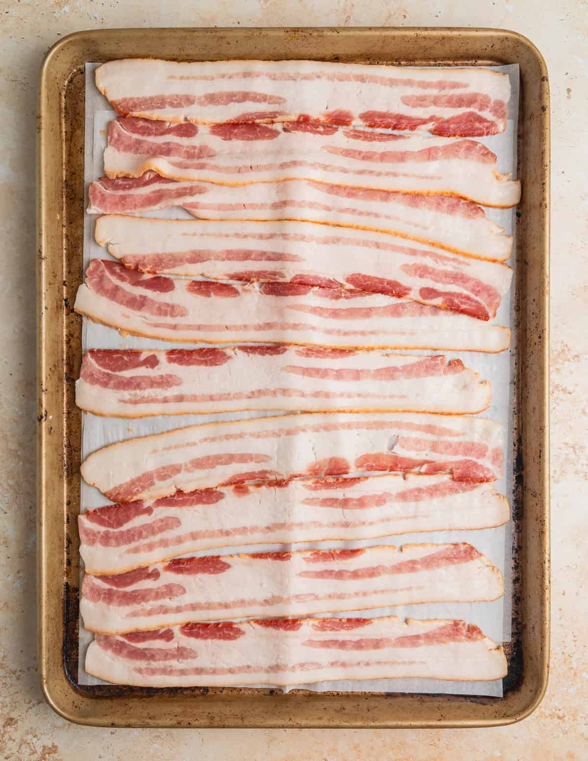 Uncooked bacon on sheetpan lined with parchment.