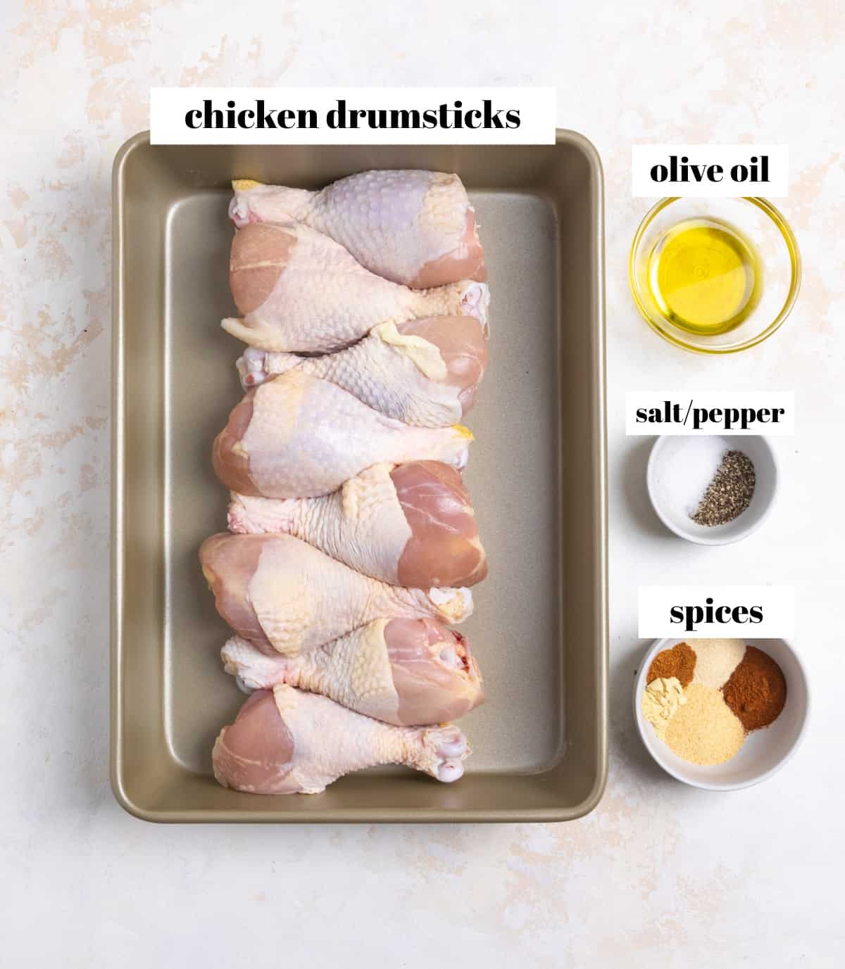 Chicken drumsticks, olive oil, and spices labeled on counter.