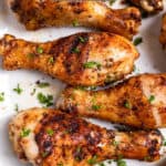 White plate with grilled chicken drumsticks topped with parsley.