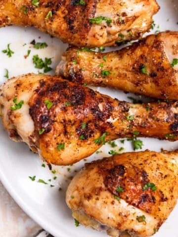 Overhead view of chicken legs grilled on white dish.
