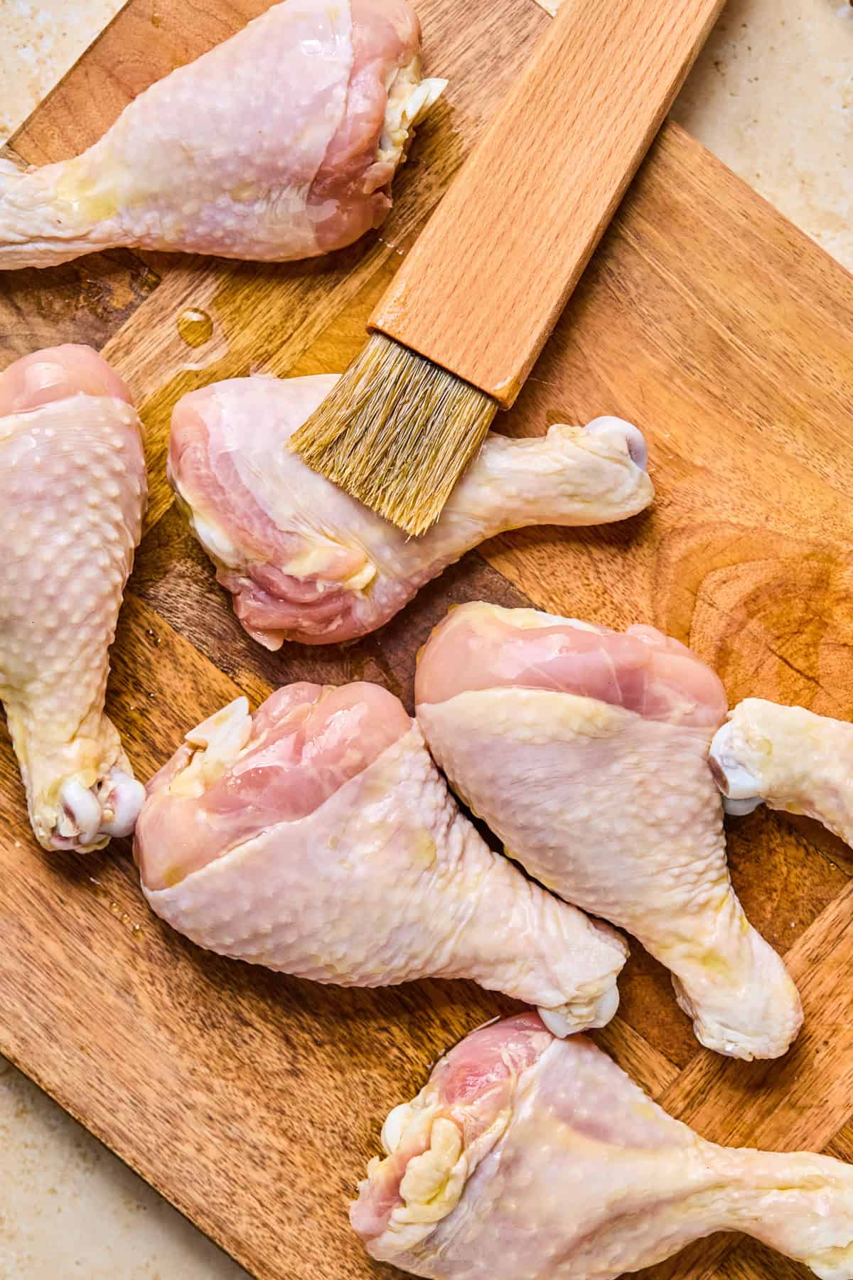 Chicken legs being rubbed by oil with brush.