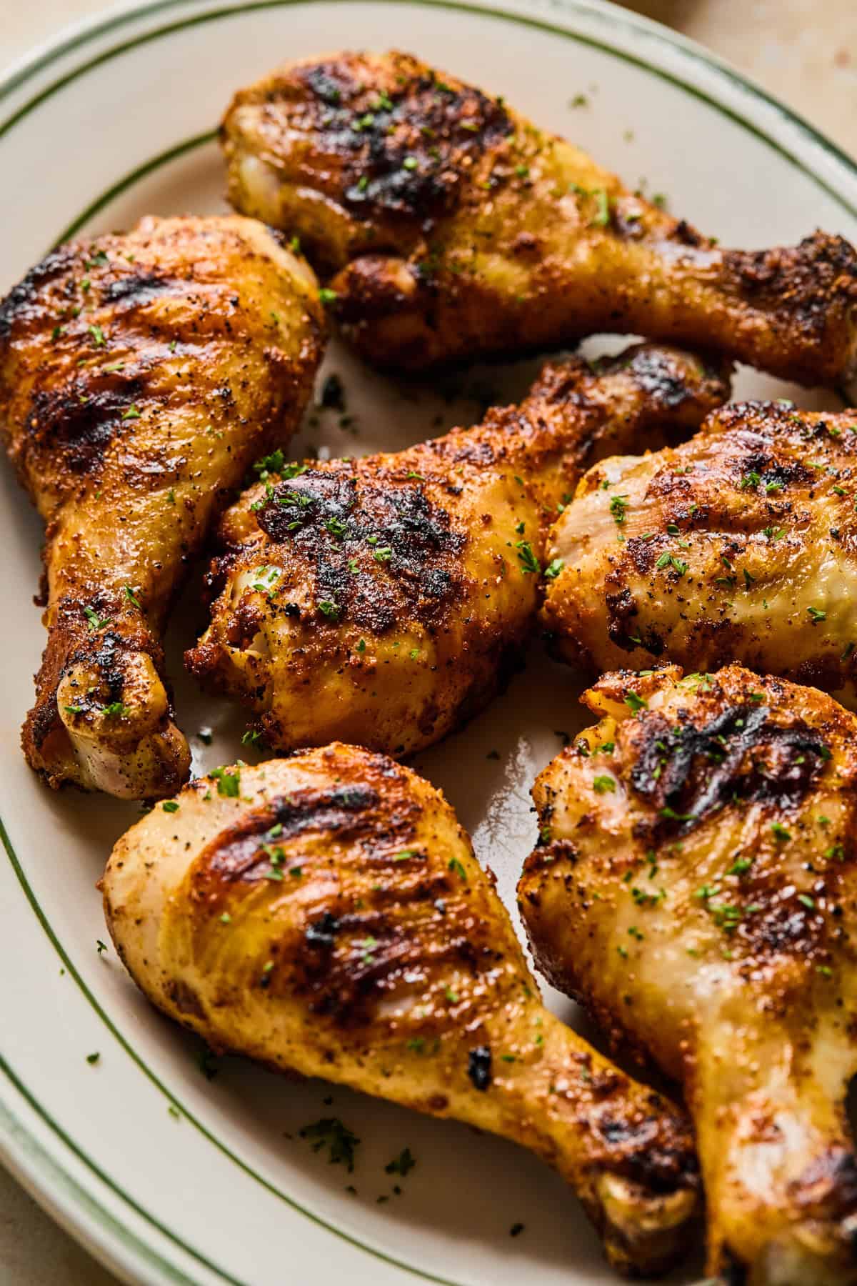 Grilled chicken legs on white dish with tongs and chopped parsley on top.