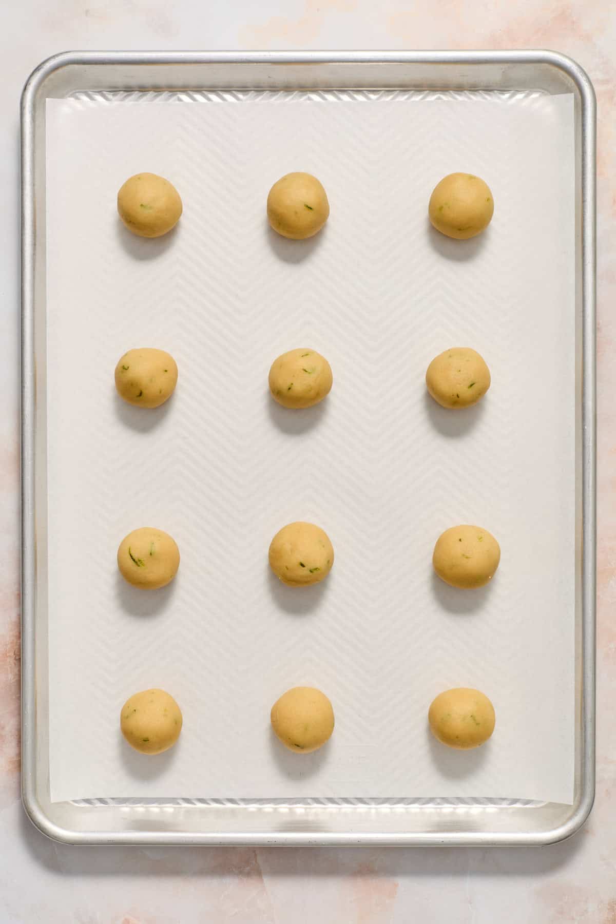 Key lime cookie dough rolled into balls on parchment lined baking sheet.