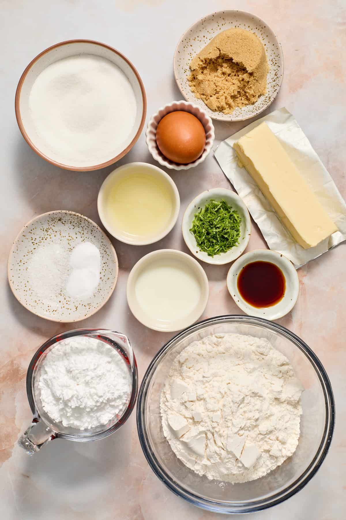 Butter, flour, sugar, vanilla, lime zest and other ingredients arranged on surface.