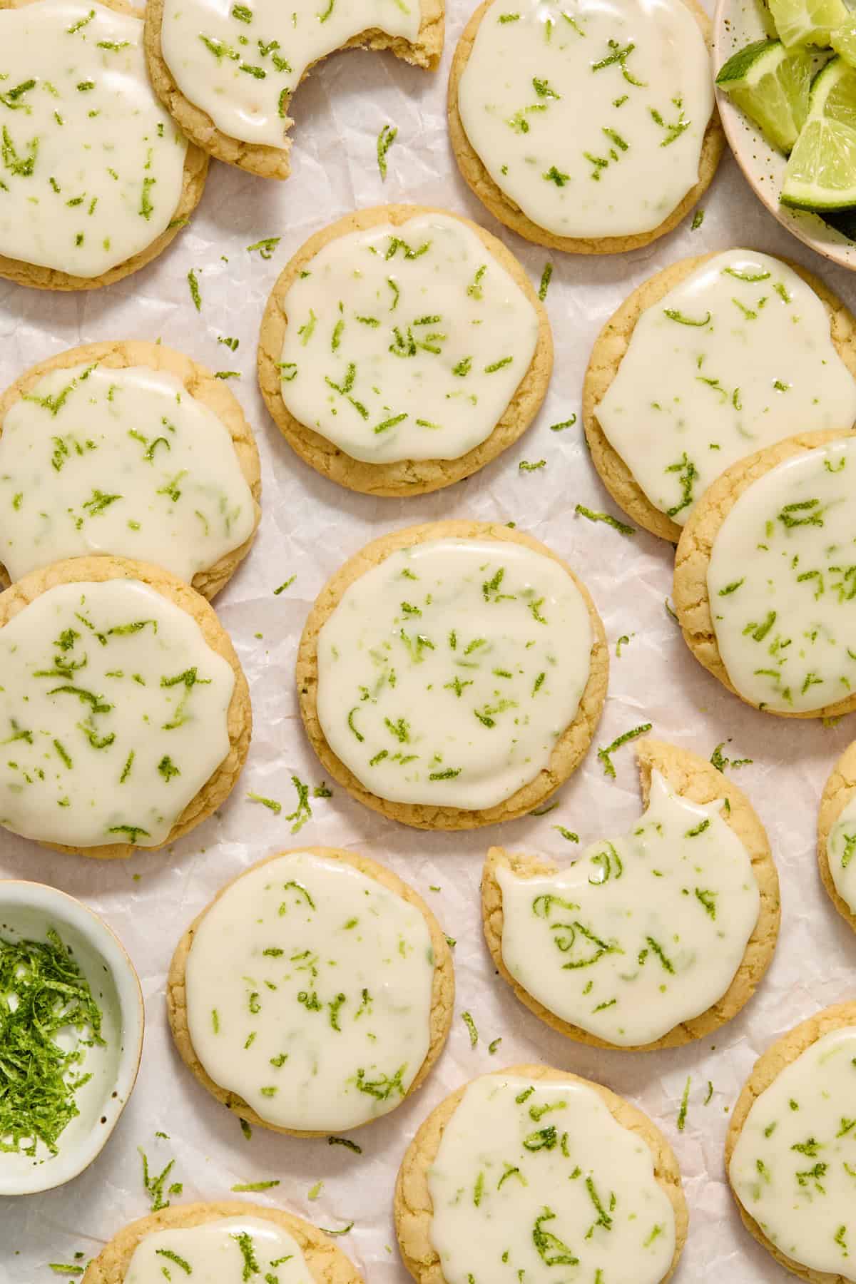Key lime cookie with lime glaze on counter with other cookies and limes surrounding.